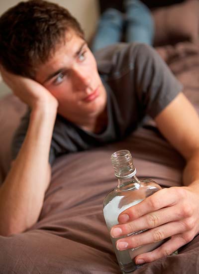 молодой парень лежит на диване с бутылкой алкоголя в руке