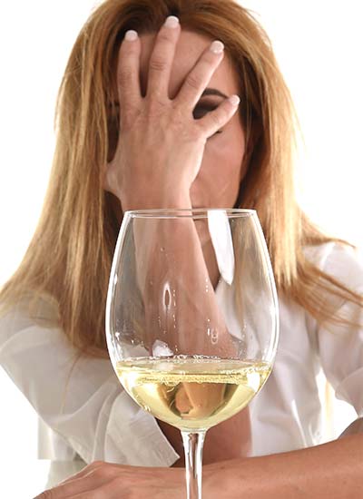 женщина сидит рядом с бокалом шампанского, закрыв лицо рукой
