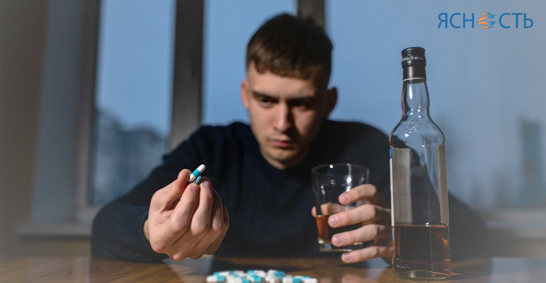 Мужчина сидит с таблетками и бутылкой алкоголя